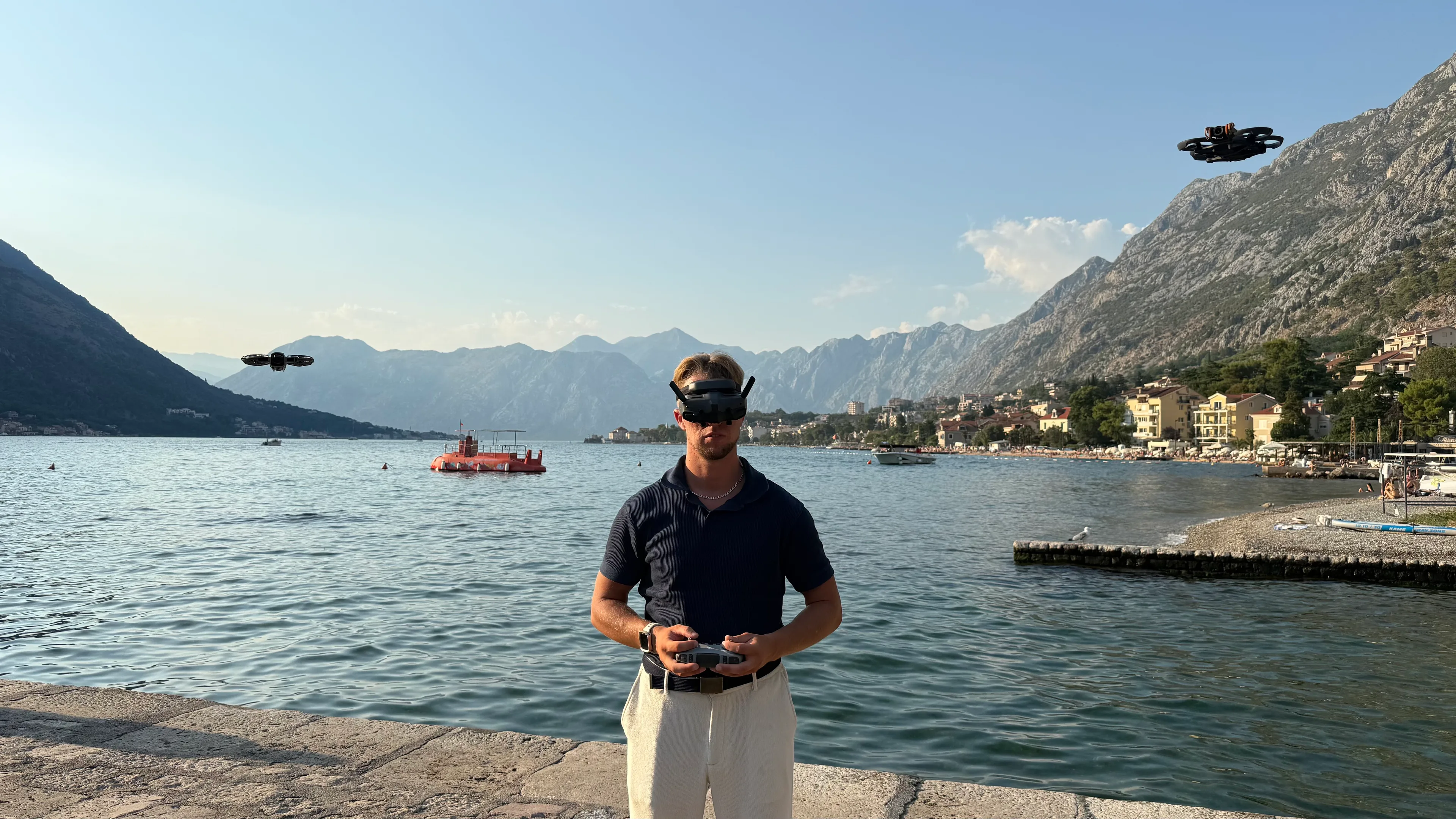 Pilot w goglach FPV na brzegu Zatoki Kotorskiej, za nim w powietrzu dwa drony